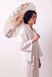 Sombrilla japonesa 'No-Kodai' abierta y sostenida por un modelo con kimono blanco — tela crema con rama florida rosa sobre fondo libre