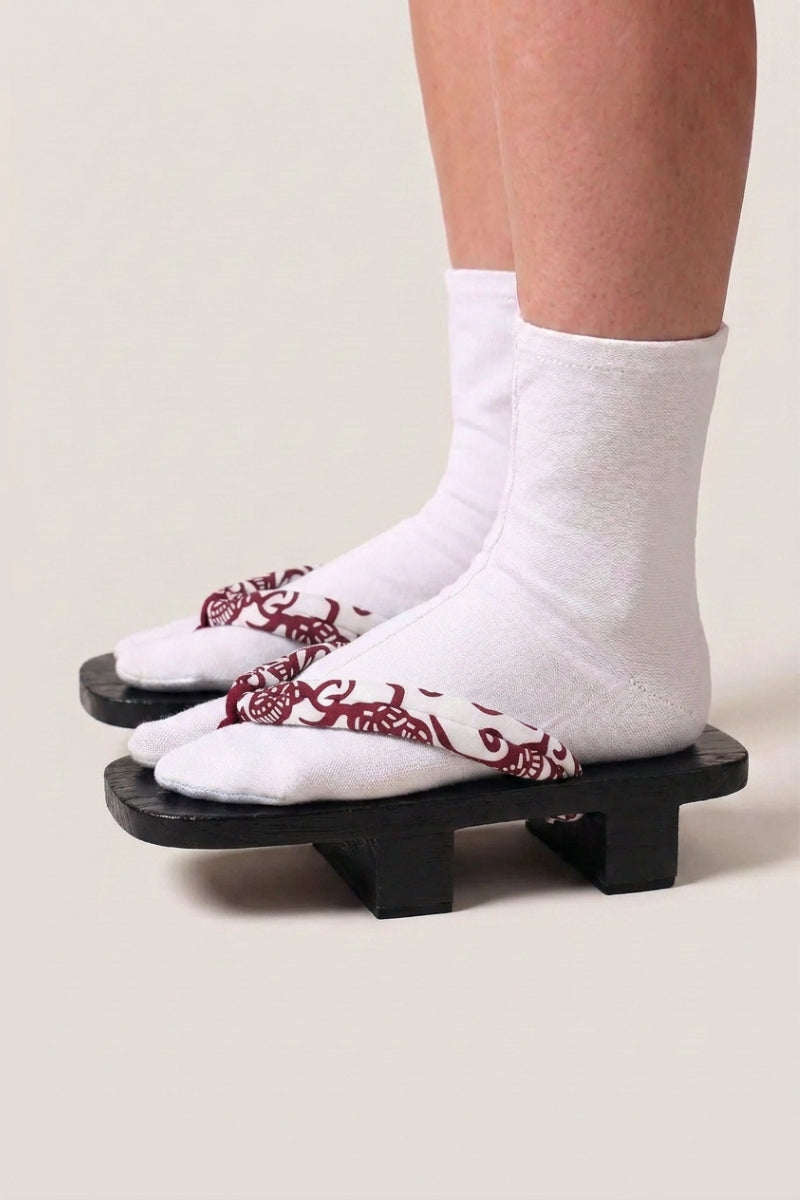 Geta japonés 'Aomori' calzada con calcetines tabi blancos, vista de perfil — plataforma de madera teñida de negro, tira roja y blanca con motivo de cachemira