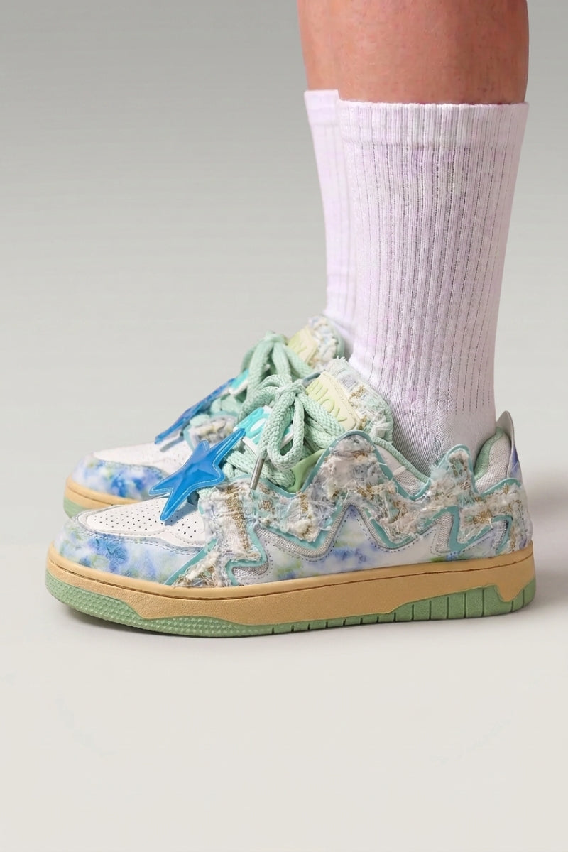 Zapatillas bajas 'Kasumi' en verde — grafiti pintado en todo el corte y suela teñida a juego, con calcetines blancos sobre fondo de estudio gris