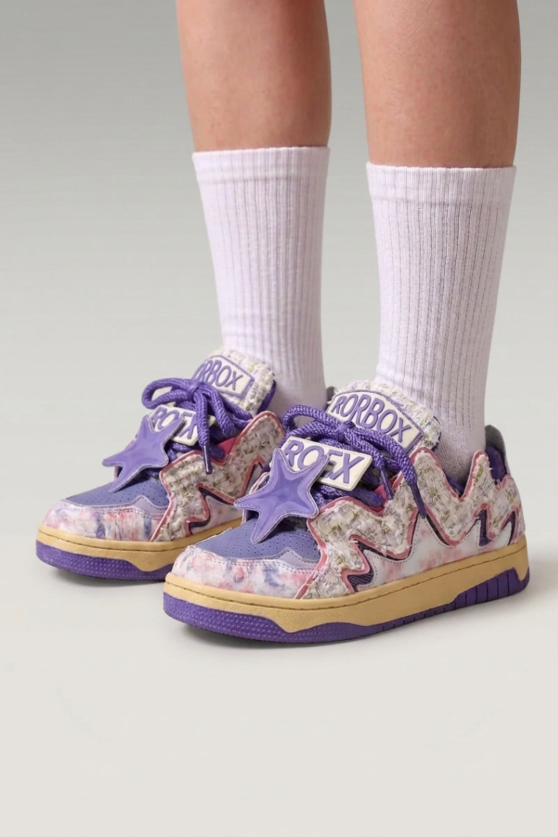 Zapatillas bajas 'Kasumi' en violeta — grafiti pintado en todo el corte y suela teñida a juego, con calcetines blancos sobre fondo de estudio gris