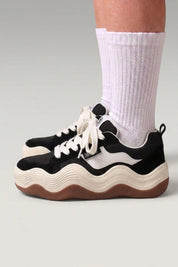 Zapatillas de plataforma 'Nami' en negro — suela de plataforma cortada en onda ondulada bicolor, con calcetines blancos sobre fondo de estudio gris