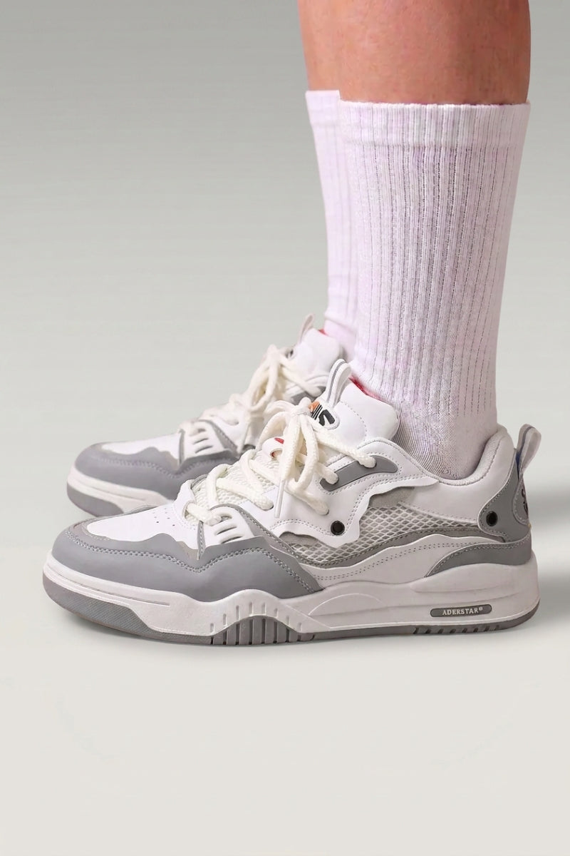 Zapatillas bajas 'Raijin' en gris — paneles de malla superpuestos y suela baja nervada, con calcetines blancos sobre fondo de estudio gris