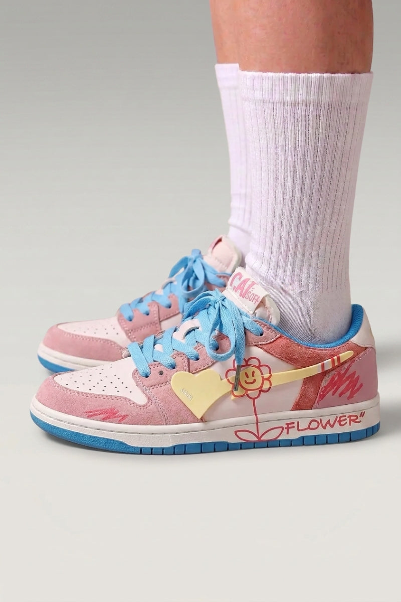 Zapatillas bajas 'Hanabi' en rosa — parches de color, flor cosida en el talón y cordones anchos, con calcetines blancos sobre fondo de estudio gris