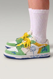 Zapatillas bajas 'Hanabi' en verde — parches de color, flor cosida en el talón y cordones anchos, con calcetines blancos sobre fondo de estudio gris