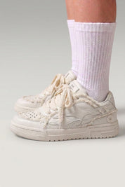 Zapatillas bajas 'Seiryu' en blanco — lona lavada con estampado floral difuminado y suela cupsole crema, con calcetines blancos sobre fondo de estudio gris