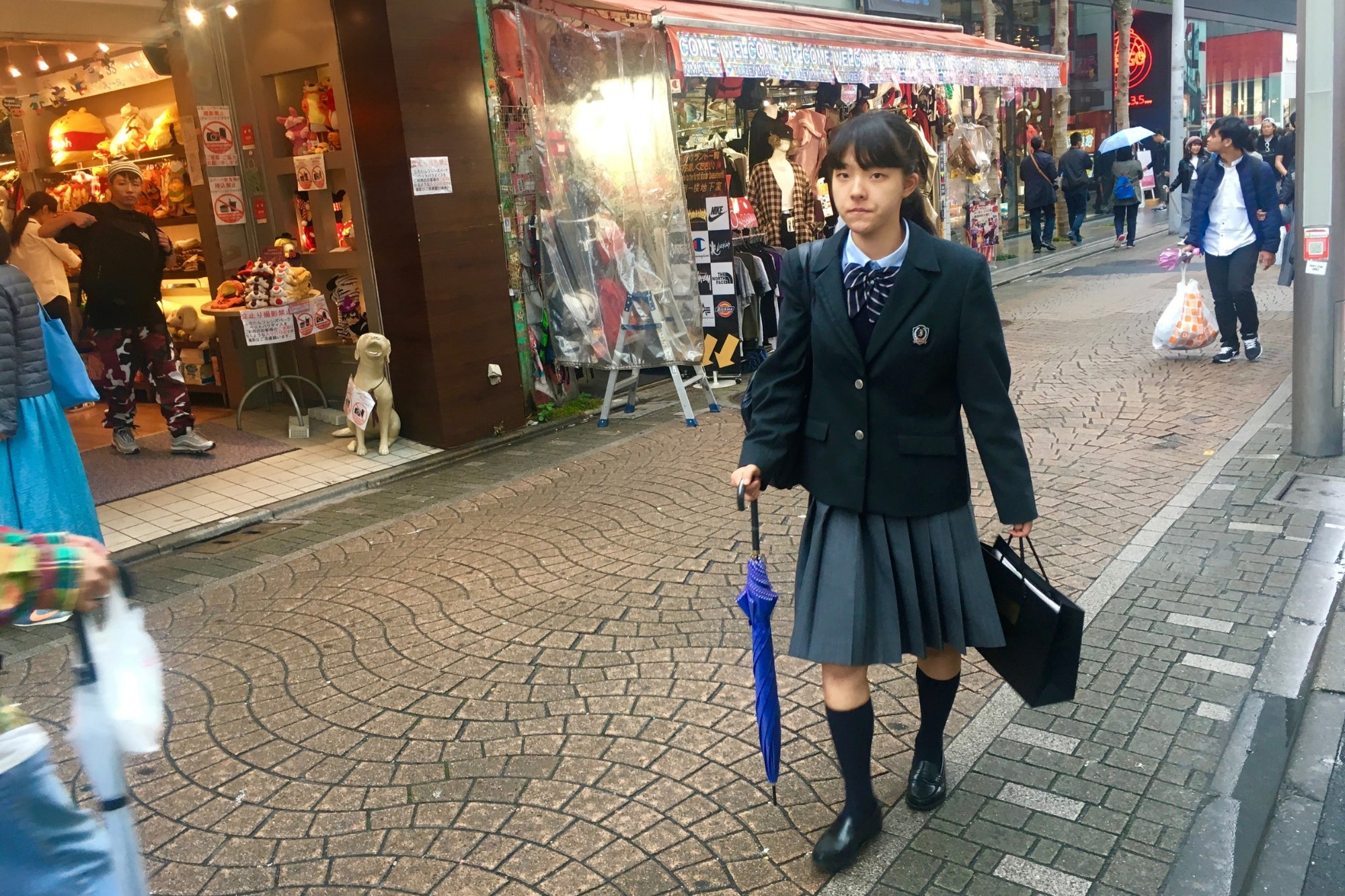 Estudiante japonesa con uniforme escolar caminando por una calle comercial de Harajuku, símbolo del estilo y de la juventud en Tokio.
