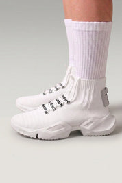 Zapatillas altas 'Kashiwa' en blanco — punto alto tipo calcetín sin cordones y suela gruesa, con calcetines blancos sobre fondo de estudio gris