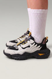 Zapatillas chunky 'Shinshiro' en blanco — líneas nervadas en los laterales y suela moteada, con calcetines blancos sobre fondo de estudio gris