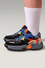 Zapatillas chunky 'Tsuruga' en negro — paneles contrastados azul y naranja y suela de goma, con calcetines blancos sobre fondo de estudio gris