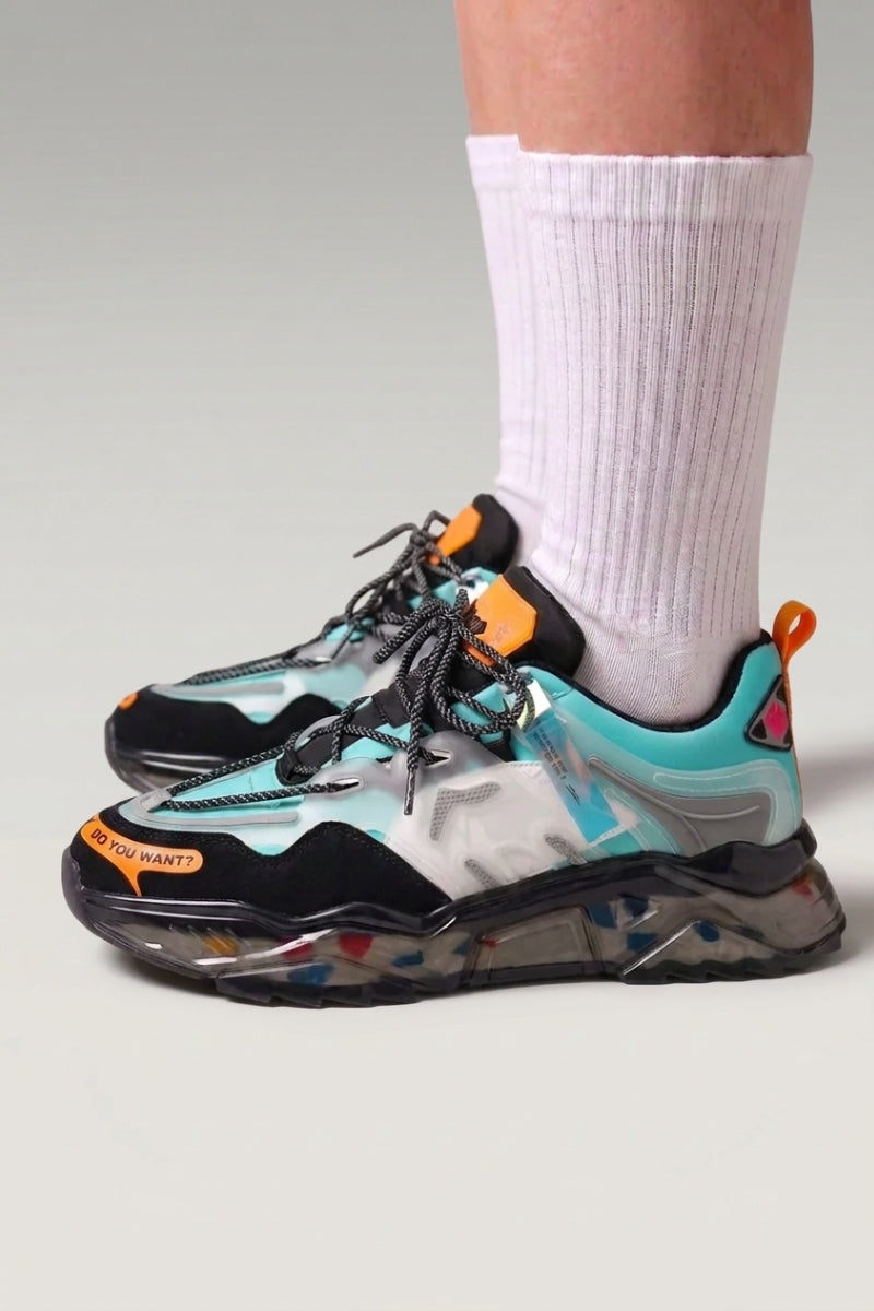 Zapatillas chunky 'Hekinan' en azul — suela translúcida sembrada de fragmentos multicolores, con calcetines blancos sobre fondo de estudio gris