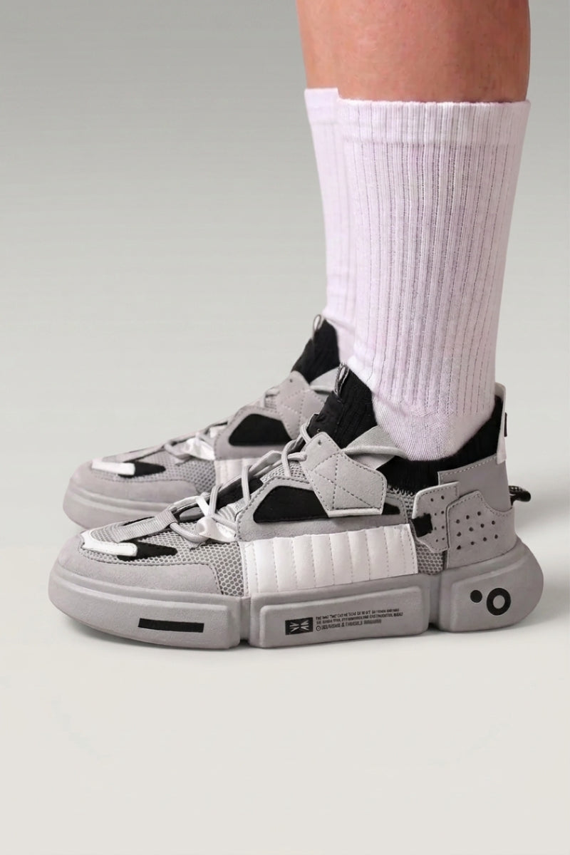 Zapatillas bajas 'Kazuno' en gris — correas utilitarias, ojales metálicos y suela segmentada, con calcetines blancos sobre fondo de estudio gris