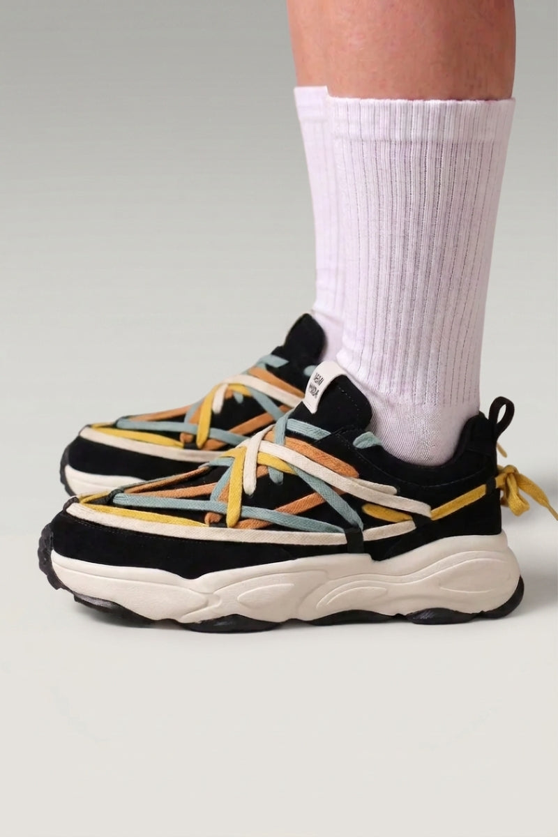 Zapatillas chunky 'Fujioka' en negro — doble cordonera multicolor y suela gruesa crema, con calcetines blancos sobre fondo de estudio gris