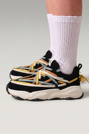 Zapatillas chunky 'Fujioka' en negro — doble cordonera multicolor y suela gruesa crema, con calcetines blancos sobre fondo de estudio gris