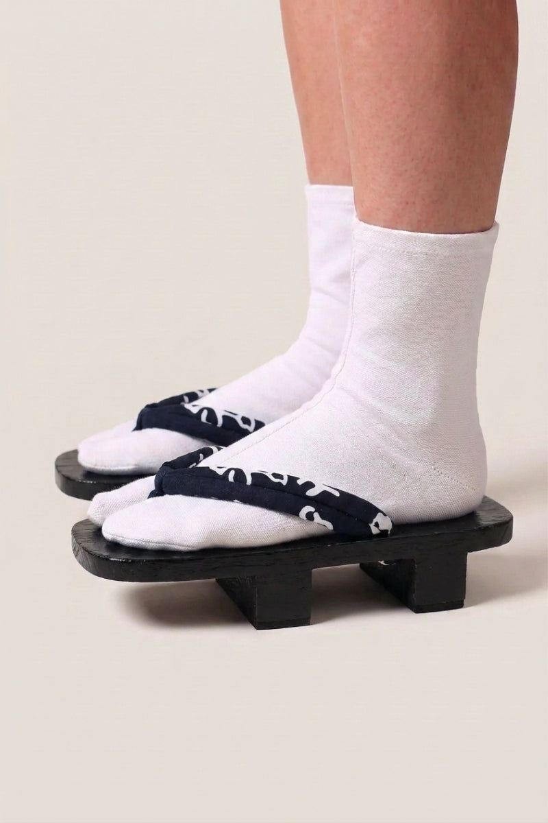 Geta japonés 'Nagano' calzada con calcetines tabi blancos, vista de perfil — plataforma de madera teñida de negro, tira azul noche con volutas blancas