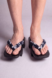 Geta japonés 'Nagano' calzada con los pies descalzos, vista frontal — tira azul noche con volutas blancas sobre plataforma alzada de madera teñida de negro