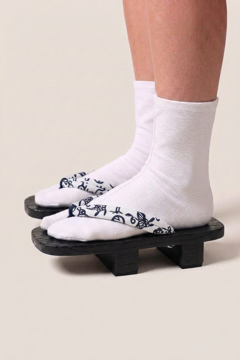 Geta japonés 'Utsomita' calzada con calcetines tabi blancos, vista de perfil — plataforma de madera teñida de negro, tira blanca con volutas azul noche